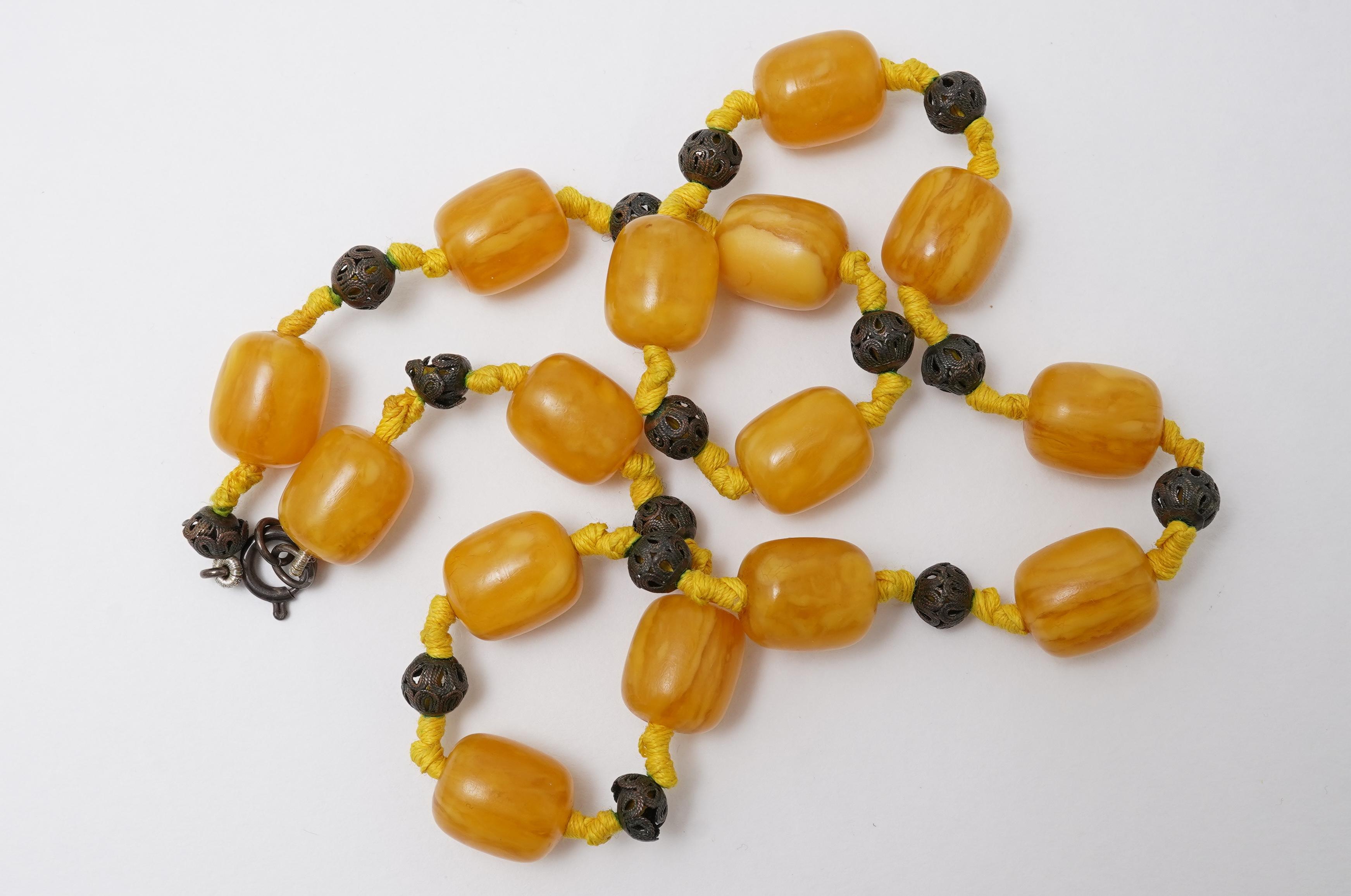 An amber necklace and carving, comprising: an amber necklace, composed of beads each measuring approximately 12 x 12 x 14mm, spaced by openwork metal beads, length 48cm; and an amber carving of a hawk on a rock, length 4